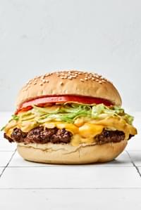smash burger on a toasted bun, layered with crisp lettuce, cooked onion, melted American cheese, and a slice of fresh tomato