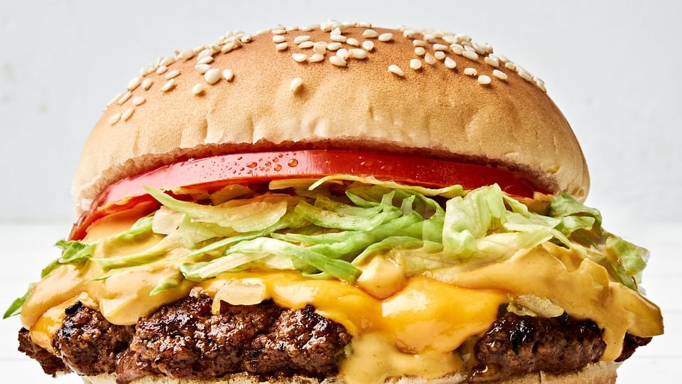 smash burger on a toasted bun, layered with crisp lettuce, cooked onion, melted American cheese, and a slice of fresh tomato