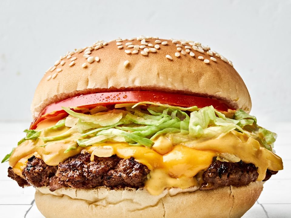 smash burger on a toasted bun, layered with crisp lettuce, cooked onion, melted American cheese, and a slice of fresh tomato