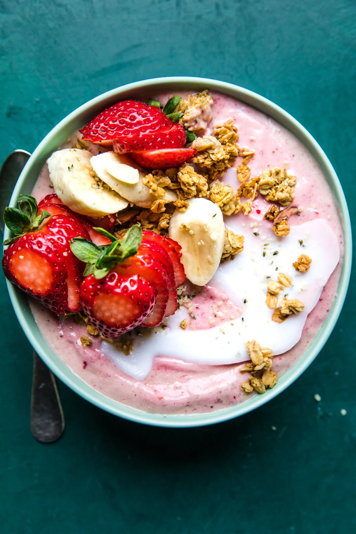 a smoothie bowl topped with strawberries, bananas, granola and a drizzle of coconut oil, in a list of healthy breakfast ideas