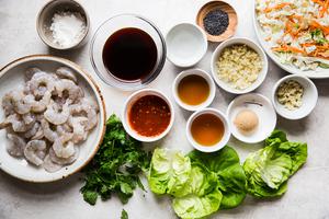 raw shrimp on a plate next to butter lettuce, cabbage slaw, cilantro, soy sauce, Sesame oil, Chili sauce, Brown sugar, honey