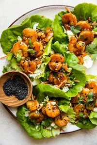 honey garlic shrimp lettuce wraps with and Asian cabbage slaw in butter lettuce on a plate with sesame seeds