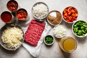 ingredients for stuffed pepper soup ground beef, bell peppers, shredded cheese in a bowl, 2 cans of fire roasted tomatoes