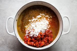rice and canned tomatoes being added to a pot full of stuffed pepper soup