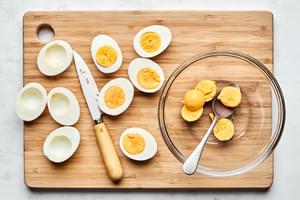 hard boiled eggs sliced in half with the yokes being scooped out with a spoon