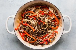 ground beef with onions and bell peppers in a large white skillet