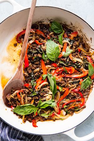 thai basil beef in a large white skillet with a wooden spoon