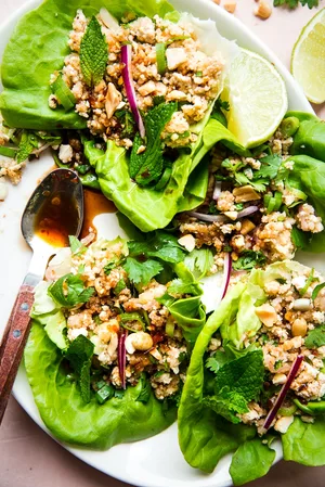 Four tofu lettuce wraps shown on a white platter next to a spoon full of seasoned soy sauce.