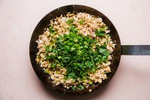 crumbled tofu, seasoned with soy sauce and other spices shown in a large metal skillet topped with fresh herbs.