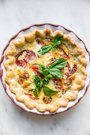 tomato, basil and caramelized onion quiche topped with parmesan in a ceramic pie pan