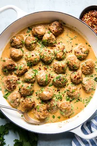 Turkey meatballs in a creamy red curry sauce topped with red pepper flakes and fresh cilantro in a skillet.