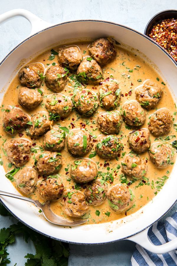Turkey meatballs in a creamy red curry sauce topped with red pepper flakes and fresh cilantro in a skillet.