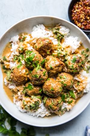 turkey meatballs in a creamy red curry sauce over white rice in a white bowl topped with fresh cilantro and red pepper flakes