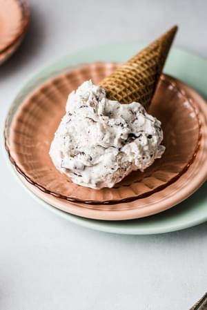 a scoop of Vegan Mint Chip Ice Cream in a cone resting on a pink plate
