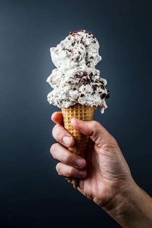 3 scoops of Vegan Mint Chip Ice Cream in a cone held by a hand