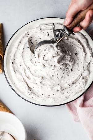 hand using an ice cream scooper to scoop Vegan Mint Chip Ice Cream out of a pie dish