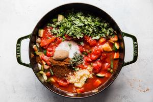 thyme, brown sugar, chili powder, salt, basil, vegetable stock, canned tomatoes added to cooked vegetables in a pot.