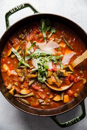 a pot of homemade vegetable soup topped with fresh basil and shaved parmesan