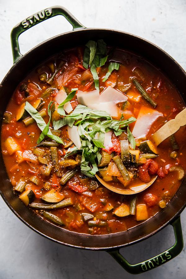 a pot of homemade vegetable soup topped with fresh basil and shaved parmesan