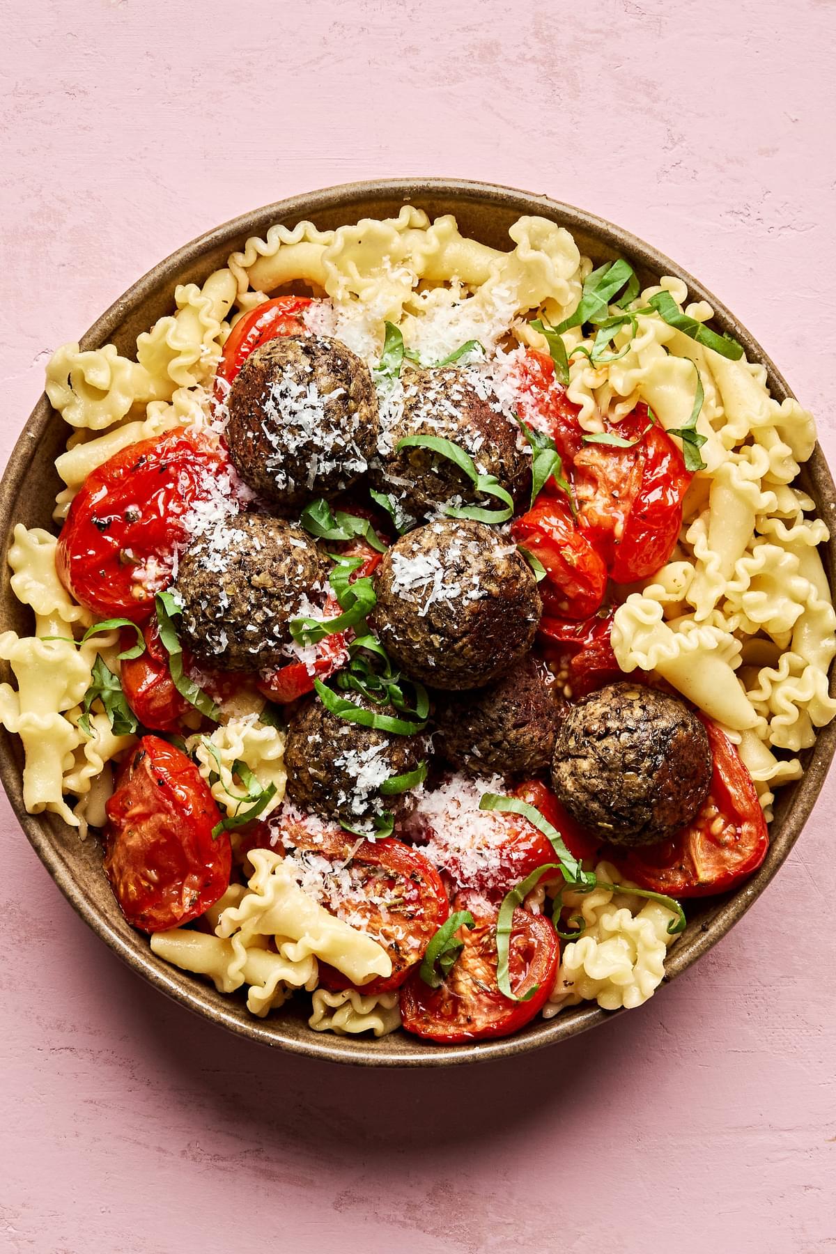 Vegetarian meatballs served over a bed of pasta noodles, topped with marinara sauce and garnished with fresh basil & Parmesan