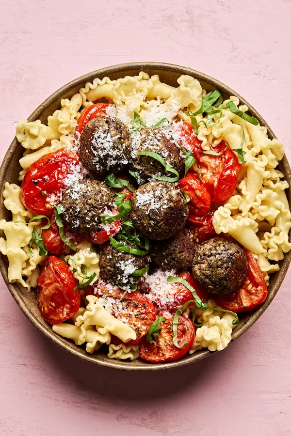 Vegetarian meatballs served over a bed of pasta noodles, topped with marinara sauce and garnished with fresh basil & Parmesan
