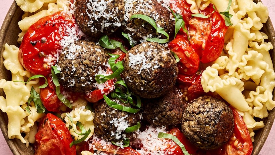 Vegetarian meatballs served over a bed of pasta noodles, topped with marinara sauce and garnished with fresh basil & Parmesan