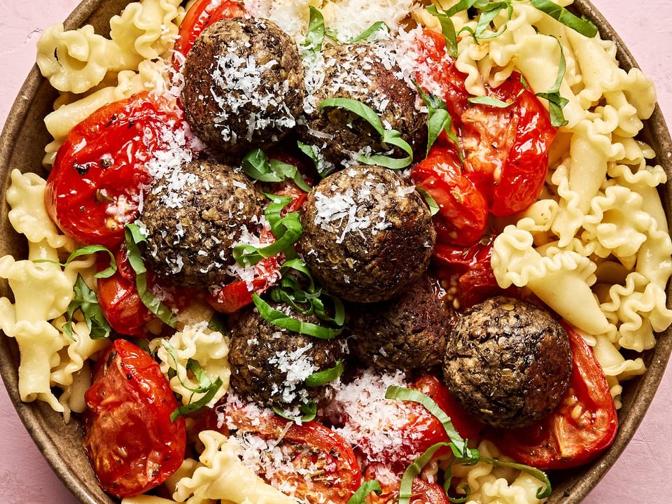 Vegetarian meatballs served over a bed of pasta noodles, topped with marinara sauce and garnished with fresh basil & Parmesan