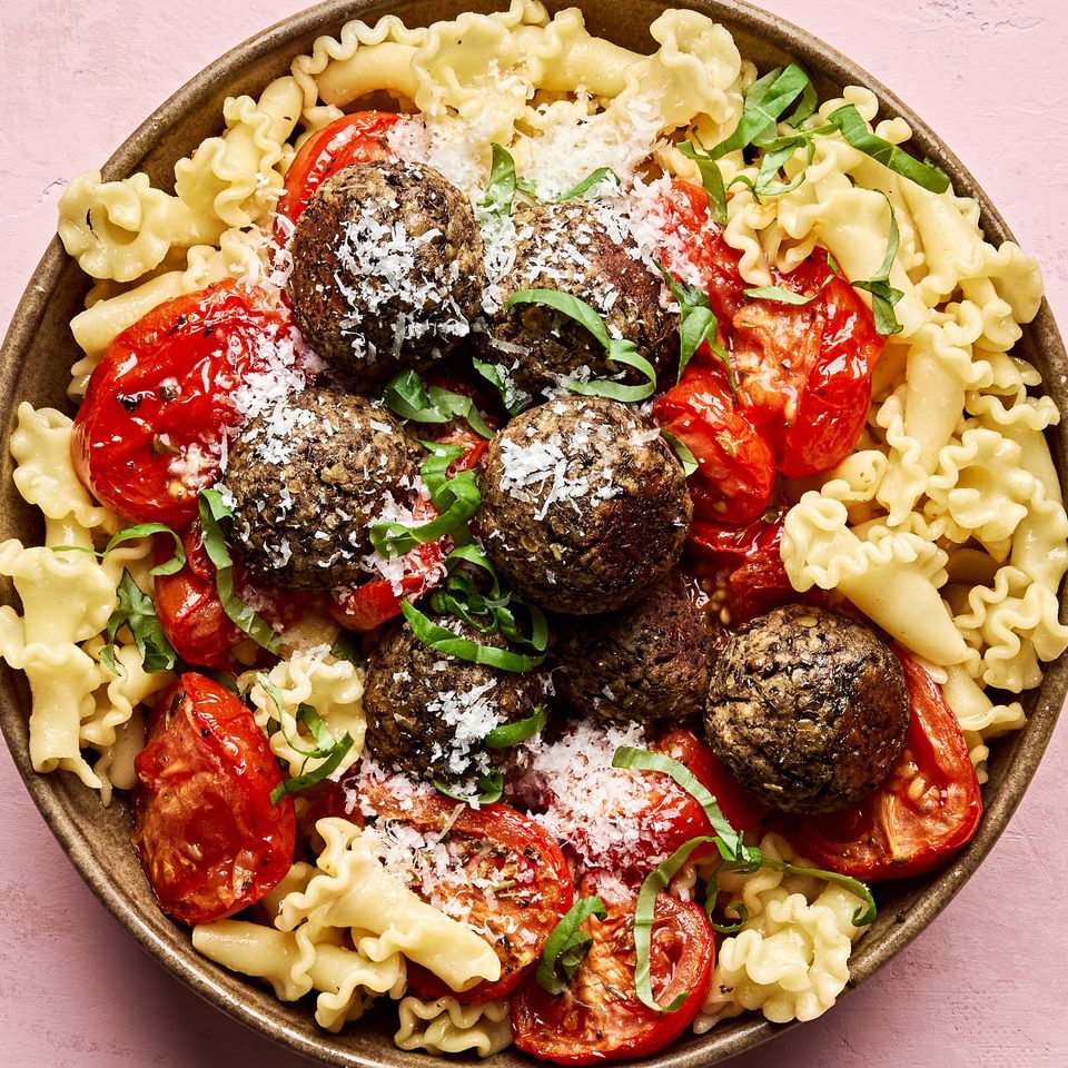 Vegetarian meatballs served over a bed of pasta noodles, topped with marinara sauce and garnished with fresh basil & Parmesan