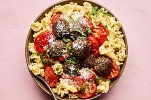 Vegetarian meatballs served over a bed of pasta noodles, topped with roasted tomatoes & garnished with fresh basil & Parmesan