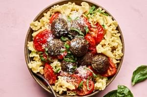 Vegetarian meatballs served over a bed of pasta noodles, topped with marinara sauce and garnished with fresh basil & Parmesan