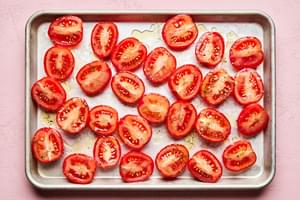 Halved Roma tomatoes tossed with olive oil, Italian seasoning and salt arranged on a baking sheet ready to roast in the oven