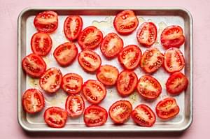 Halved Roma tomatoes tossed with olive oil, Italian seasoning and salt arranged on a baking sheet ready to roast in the oven