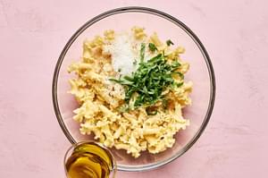 Pasta being tossed with olive oil, fresh basil and Parmesan cheese to later be topped with tomatoes and vegetarian meatballs