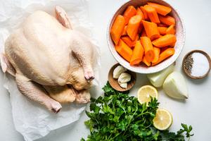 carrots, whole chicken, lemon slices, onions, salt, pepper, garlic and parsley shown in small bowls