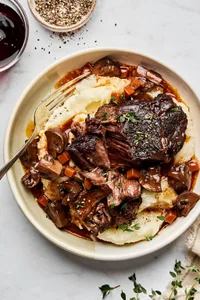 Wine-braised beef with sautéed mushrooms served over creamy mashed potatoes, garnished with fresh herbs for a hearty dinner