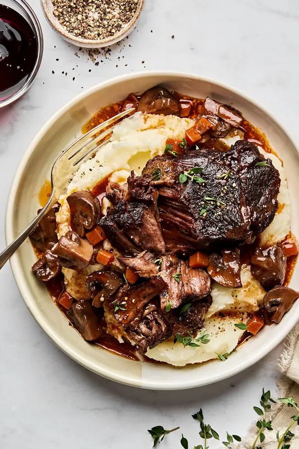 Wine-braised beef with sautéed mushrooms served over creamy mashed potatoes, garnished with fresh herbs for a hearty dinner