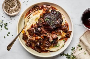 Wine-braised beef with sautéed mushrooms served over creamy mashed potatoes, garnished with fresh herbs for a hearty dinner