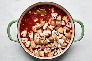 mushrooms being added to a wine and tomato sauce to make wine braised beef with mushrooms