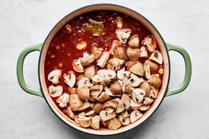 mushrooms being added to a wine and tomato sauce to make wine braised beef with mushrooms