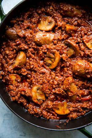 homemade spaghetti sauce shown in a large pot with sausage and mushrooms.