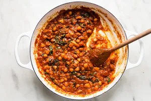 braised chickpeas with chard shown in a large white skillet with a wooden spoon