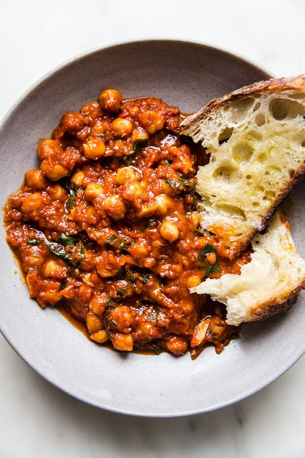 braised chickpeas in a tomato sauce with chard shown in a ceramic bowl with crusty bread