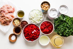 ingredients for coconut curry soup in small bowls including red peppers, raw chicken, coconut milk, kale, chicken broth