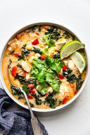 white bowl of red curry chicken soup topped with fresh cilantro and lime sliced