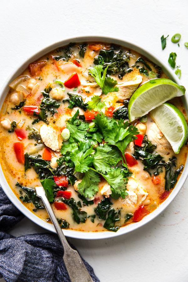 bowl of coconut curry soup with chickpeas, chicken and kale in a bowl topped with fresh cilantro and fresh lime wedges