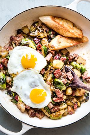 corned beef hash in a skillet topped with 2 fried eggs and served with toasted crusty bread