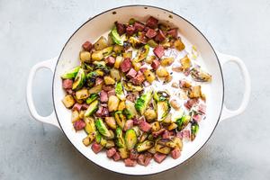 corned beef hash cooking in a pan with potatoes, shallots, brussels sprouts, cream, worcestershire and spices