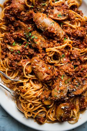 homemade spaghetti sauce with noodles and sausage on a white platter with serving spoon