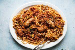 homemade spaghetti sauce with pasta noodles and sausage on a white platter with serving spoon
