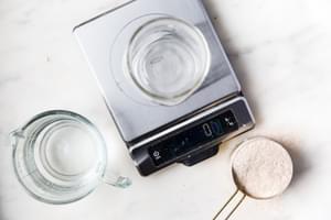 items on the counter to make sourdough starter: food scale, whole wheat flour, water and a glass jar